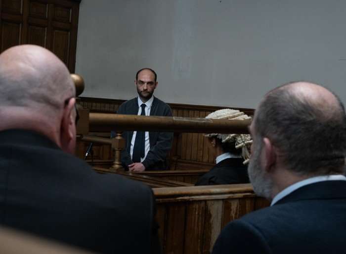 Paddy and Bear stare over towards Simo in the court room in Emmerdale