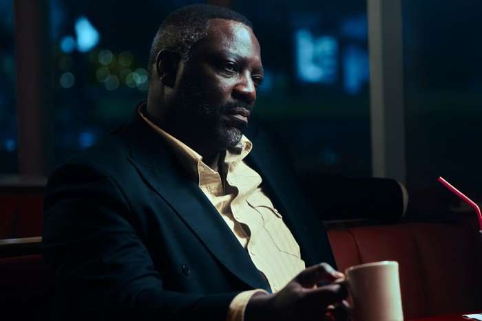 Adewale Akinnuoye-Agbaje seated in a diner as Alamo Brown in Euphoria season 3.