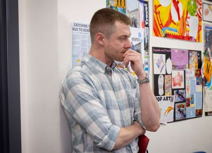 Daniel Osbourne stands with his hand on his mouth looking shocked in the school corridor in Coronation Street