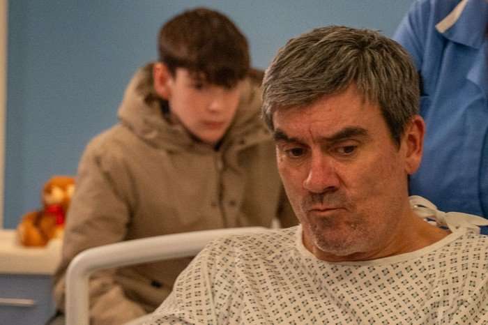 Kyle watches Cain being pushed through a hospital corridor in his wheelchair in a scene from Emmerdale
