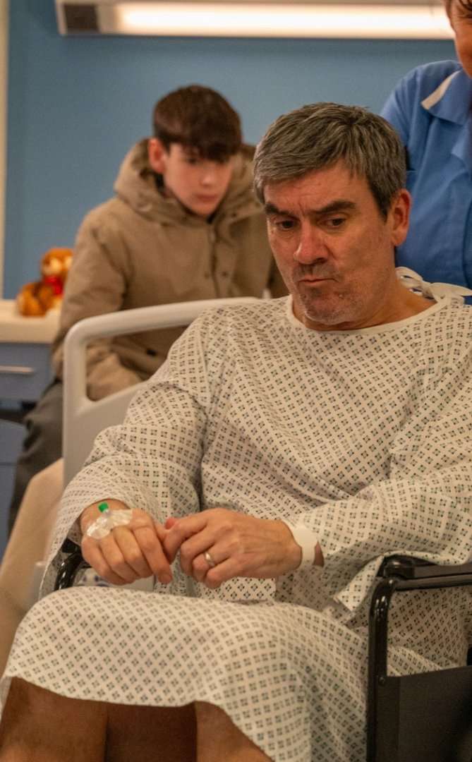 Kyle watches Cain being pushed through a hospital corridor in his wheelchair in a scene from Emmerdale