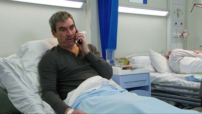 Cain lies in a hospital bed on a phone in Emmerdale
