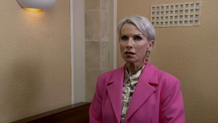 Debbie Webster stands in a pink blazer in a court in a scene from Coronation Street