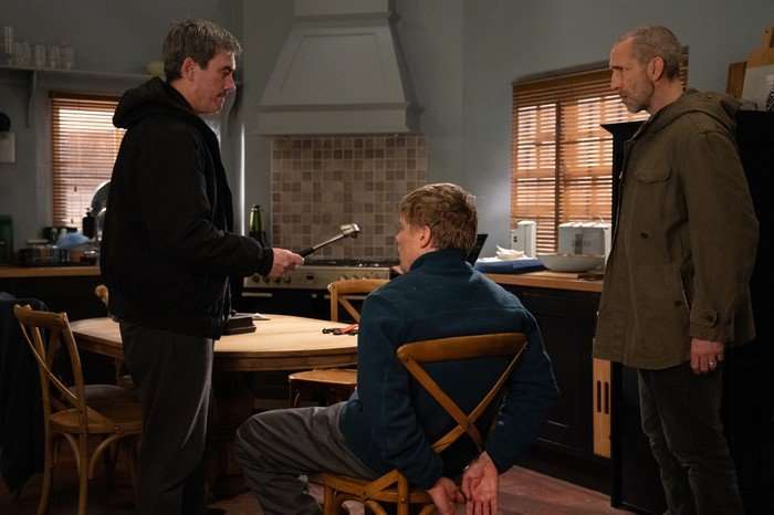Cain holds a hammer to Robert, who is strapped to a chair as Sam watches on in Emmerdale
