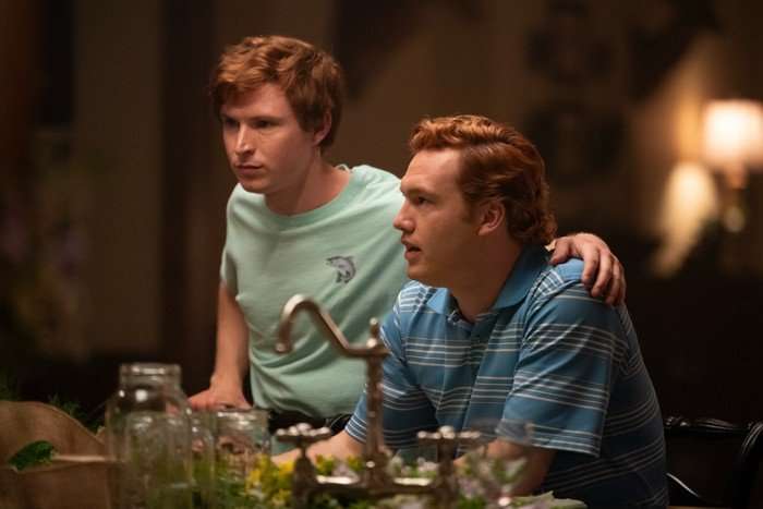 Johnny Berchtold as Paul Murdaugh and Will Harrison as Buster Murdaugh, next to one another in a kitchen. Paul is stood up with his arms around Buster, who is sat down