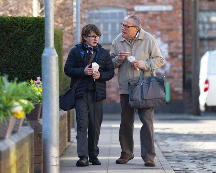 Sam and Roy walk along the street with chips in their hands in Coronation Street