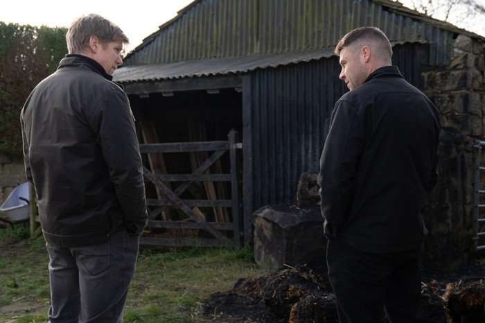 Aaron and Robert look towards a burnt out barn in a scene from Emmerdale