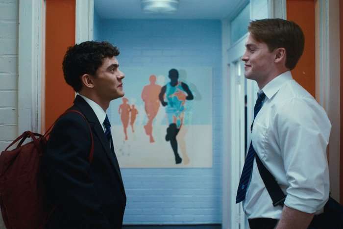 Charlie and Nick stare at each other lovingly in a hallway, wearing school uniforms