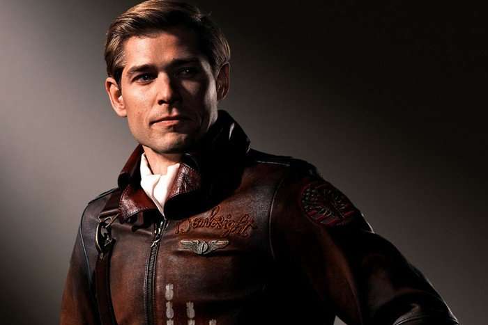 A blonde man in a brown leather airman jacket poses for the camera