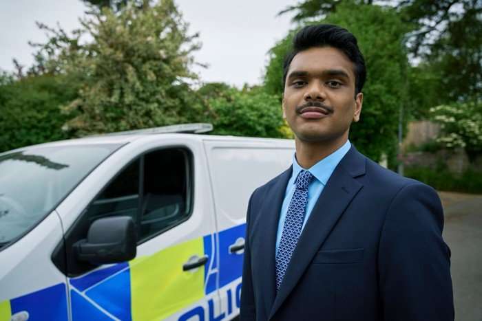 Rithvik Andugula plays DC Evan Chaudhry in Death Valley, standing in a suit in front of a police van