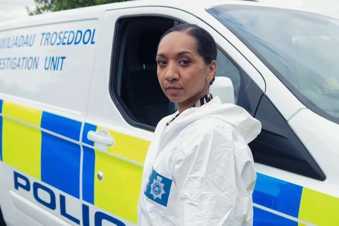 Alexandria Riley plays Baxter in Death Valley, wearing forensics gear and standing in front of a police van