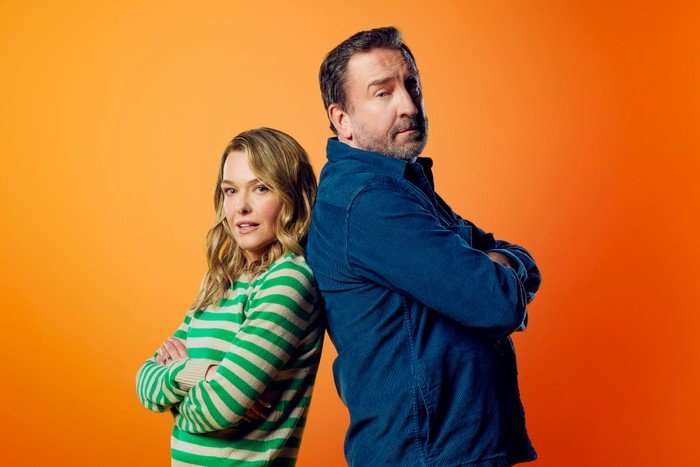 Lee Mack as Lee and Sally Bretton as Lucy in Not Going Out, photographed in a studio standing back-to-back with their arms crossed