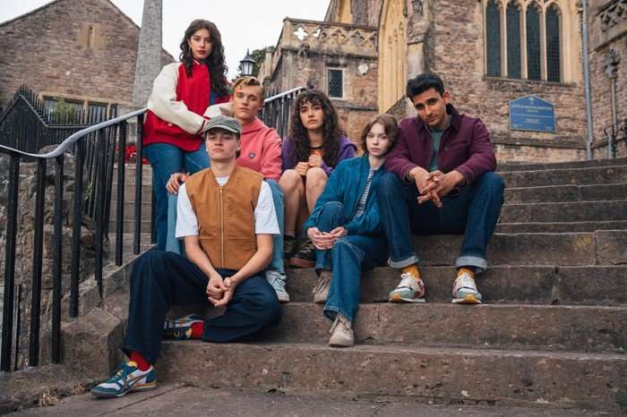 Yali Topol Margalith as Lauren, Jude Morgan-Collie as Connor Reynolds, Eden Hambleton Davies as Jamie Reynolds, Asha Banks as Cara Ward, Emma Myers as Pip Fitz-Amobi and Zain Iqbal as Ravi Singh all stood on steps outside, posing for a photo and looking ahead.