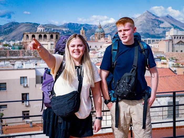 558177,TITLE:Race Across the World - Series 6 Katie and Harrison stood next to each other looking ahead of them as Katie points outwards.