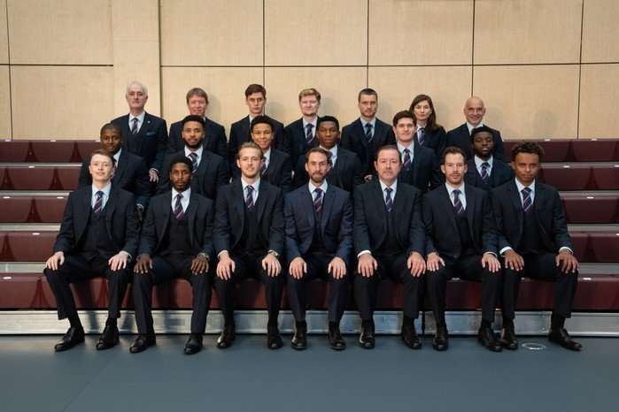 The cast of Dear England, sat in three rows wearing suits for a team photo.