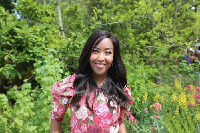 Angellica Bell stood in a garden, smiling ahead wearing a pink floral dress.