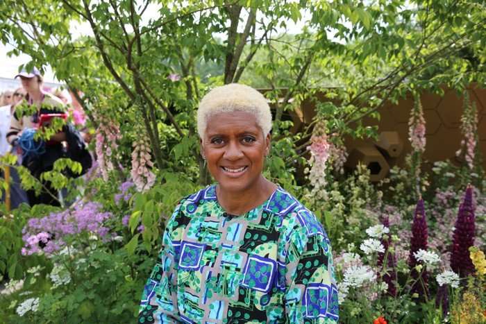 Arit Anderson stood in a garden wearing a blue and green floral blouse.