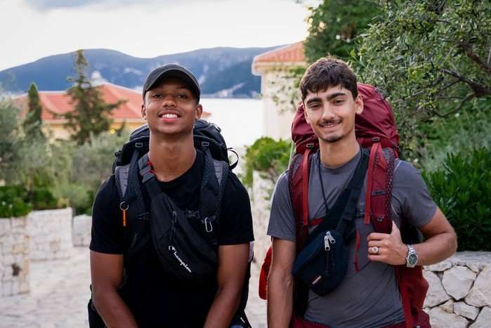560425,TITLE:Race Across the World - Series 6 Jo and Kush stood next to each other smiling ahead with large rucksacks on their back.