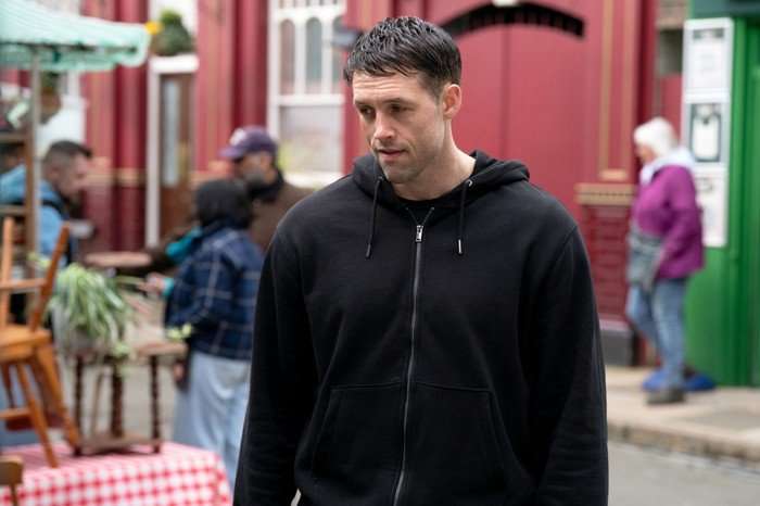 Mark stands in a black hoody in front of The Queen Vic in EastEnders