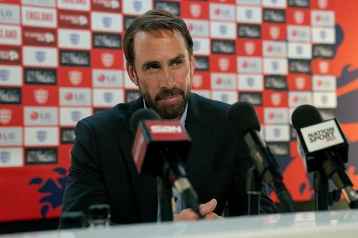 Joseph Fiennes as Gareth Southgate in Dear England Joseph Fiennes as Gareth Southgate in Dear England, sat behind microphones at a desk.