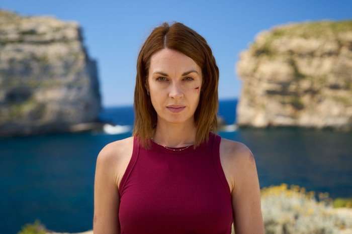 561636,TITLE:Two Weeks In August Jessica Raine as Zoe in Two Weeks in August, wearing a red top, stood by a cliff and looking at the camera.