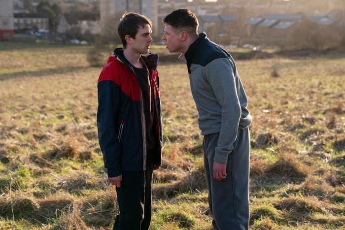 Mitchell Robertson as Young Niall and Stuart Campbell as Young Ruben in Half Man, stood in a field together. Ruben is squaring up to Niall, putting his face close to him.