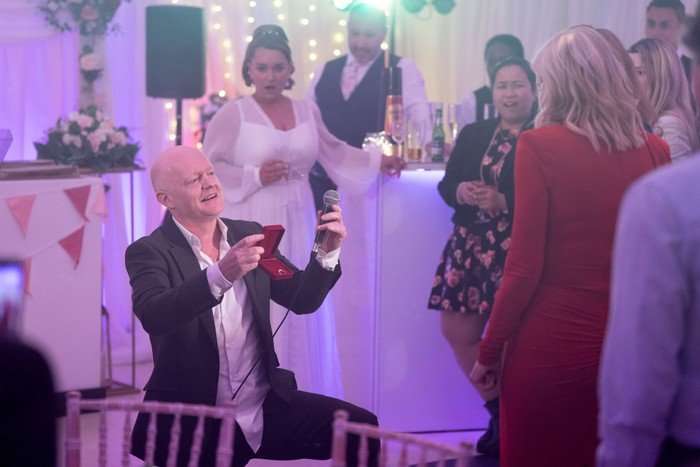563279,TITLE:Eastenders Max Branning, on one knee, holding a ring in a box and a microphone in a scene from EastEnders