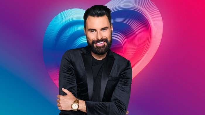 Rylan Clark wearing a black suit with his arms folded in front of his chest.