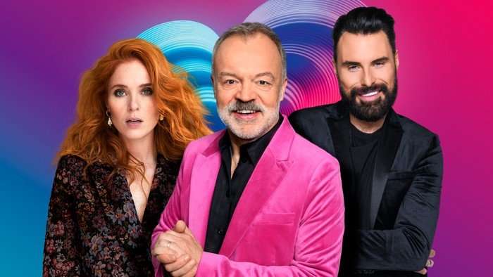 Angela Scanlon, Graham Norton and Rylan posed next to one another smiling for a photo in front of a pink Eurovision background.