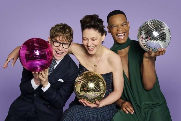 566901,TITLE:Strictly Come Dancing 2026 Johannes Radebe, Josh Widdicombe, and Emma Willis pose in front of a purple background.