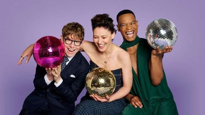 Johannes Radebe, Josh Widdicombe, and Emma Willis pose in front of a purple background.