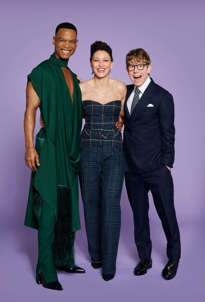 Johannes Radebe, Josh Widdicombe, and Emma Willis pose in front of a purple background.