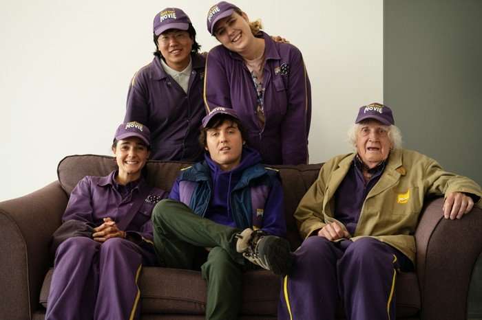 Jess (Lara Ricote), Sebastian (Aaron Chen), Sam Campbell (As himself), Pat (Helen Bauer) and Winnie (David Hargreaves) in Make That Movie Jess (Lara Ricote), Sebastian (Aaron Chen), Sam Campbell (As himself), Pat (Helen Bauer) and Winnie (David Hargreaves) all stood and sat around one another, smiling ahead.