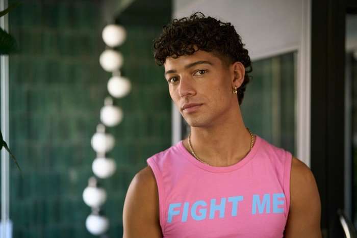 Gabriel Clark as Mikey in Tip Toe. He is standing in a bar, wearing a pink tank top that says 'FIGHT ME' across the front