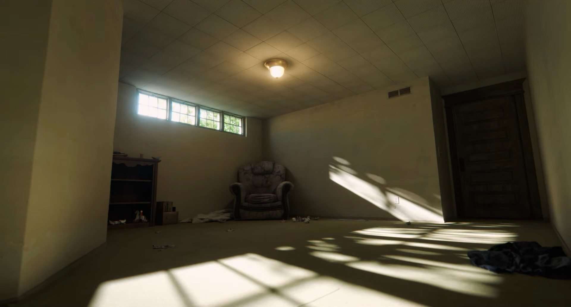 An empty room with a sofa chair and a book self inside in A24's The Backrooms.