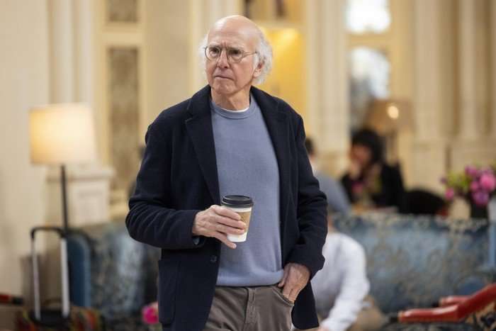 Curb Your Enthusiasm Larry David holding a coffee cup with his hand in his pocket, standing up in the middle of a store.