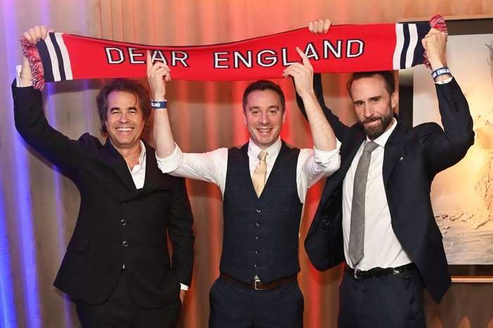 Rupert Goold, James Graham and Joseph Fiennes holding up a scarf that reads 'Dear England' above their heads and smiling.