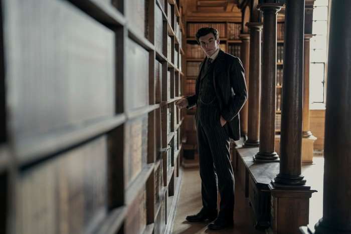 Dónal Finn as James Moriarty in Young Sherlock, stood by a bookcase, wearing a suit and looking at the camera, with his hands in his pockets.