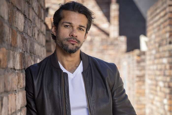 Idris Nazir stood in the Coronation Street ginnel wearing a white t-shirt and black leather jacket