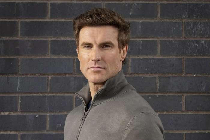 James Cartwright poses against a grey brick wall as Theo Silverton for Coronation Street.