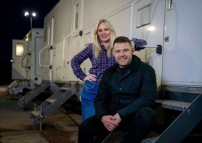 Danny Miller and Vicky Myers sit beside some trailers in a darkened carpark for filming of Corriedale