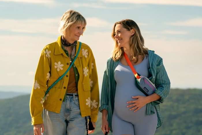 THE FOUR SEASONS, SEASON 2 Anne and Ginny stand next to each other, the former looking down at the latter's baby bump. The background is a pale blue sky with light clouds.