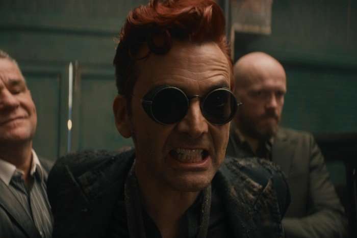 David Tennant as Crowley in Good Omens, snarling, with two bald men behind him.