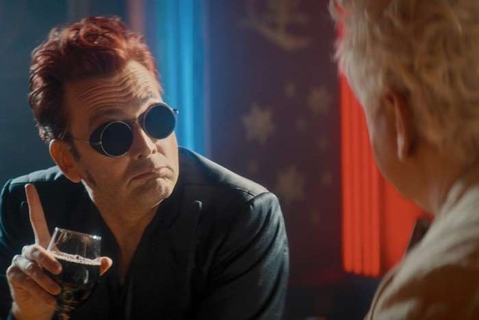 David Tennant as Crowley in Good Omens season 3 David Tennant as Crowley in Good Omens season 3, with red hair and black sunglasses, holding a glass and looking at Michael Sheen's Aziraphale.