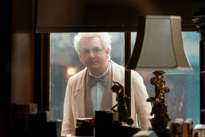 Michael Sheen as Aziraphale in Good Omens season 3 Michael Sheen as Aziraphale in Good Omens season 3, clad in white and peering through a window in