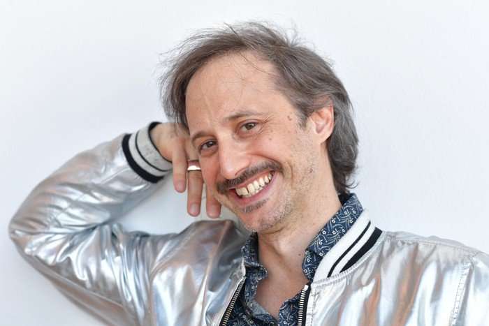 Michael Ostrowski smiling with his hand resting on the side of his head.