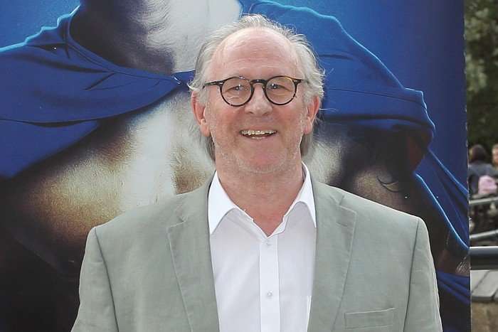 Peter Davison wearing a grey suit jacket and white shirt, and smiling.