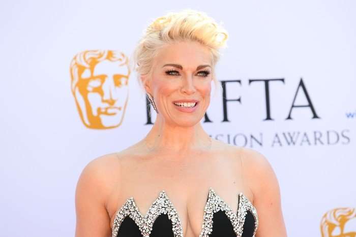 Hannah Waddingham smiling ahead in front of a white BAFTA TV Awards logo. She has blonde hair that is pinned up in an up do.