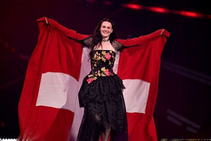 Swiss singer Zoe Me walking on stage with her arms in the air with a Swiss flag draped around her arms.