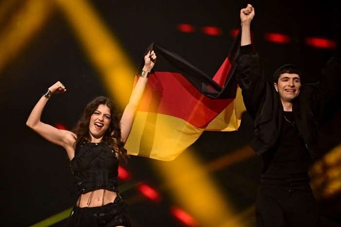 Abor & Tynna walking on stage next to each other, holding up the German flag.